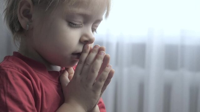 little daughter girl makes a wish prayers bedtime religion concept . prayer child indoors praying by bed front of window lifestyle