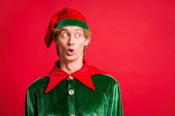 Photo of astonished elf guy look into empty space wear green costume pointy hat isolated over red...