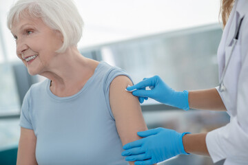 Fototapeta premium Nurse making an injection to an elderly smiling woman
