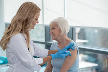 Long-haired smiling nurse making vaccination to an elderly woman - obrazy, fototapety, plakaty
