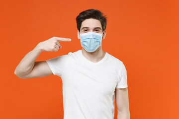 Young man 20s wearing casual white t-shirt pointing index finger on sterile face mask to safe from...