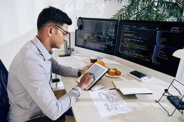 Serious young Indian software developer checking mindmap on tablet computer when planning work on...