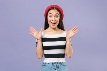 Obraz na płótnie Canvas Excited surprised young brunette asian woman wearing striped t-shirt red beret standing keeping mouth open spreading hands looking camera isolated on pastel violet colour background studio portrait.