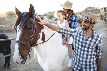 Happy parents with daughter riding a horse at farm ranch - Family lifestyle and animal love concept...