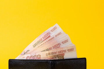 Black leather wallet opened, filled with a fan of five thousand rubles. Yellow background. Close...