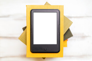 Reading and knowledge. E-book reader is on top of a stack of books on a wooden background. Flat...