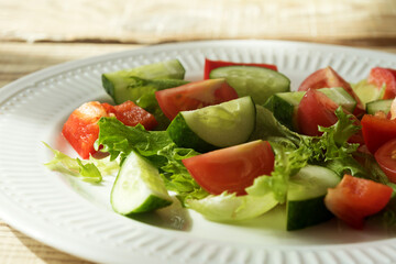 salad of fresh vegetables tomato cucumber and sweet pepper in a white plate on a wooden table