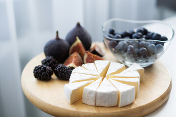 Camembert cheese, figs, blueberries and blackberries on a wooden round Board