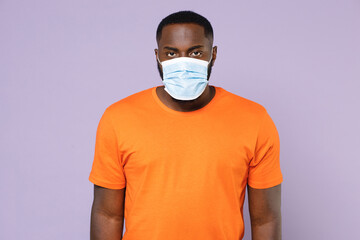 Young african american man 20s in basic casual orange t-shirt sterile face mask to safe from coronavirus virus covid-19 during pandemic quarantine isolated on pastel violet background studio portrait.