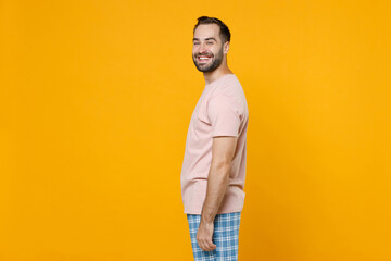 Side view of smiling young bearded man 20s in pajamas home wear looking camera while resting at...