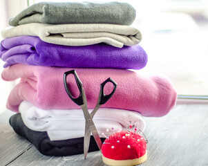 Multi-colored fabrics are stacked on top of each other. Tailors scissors and pins are ready for...