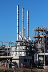 Old partially renovated and modernized oil refinery industrial complex with three shiny new metal industrial chimneys rising above dense metal construction on clear blue sky background