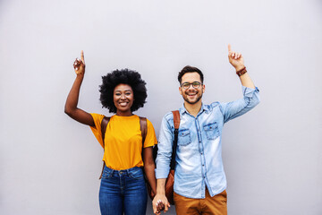 Young attractive multiracial couple holding hands and pointing up.