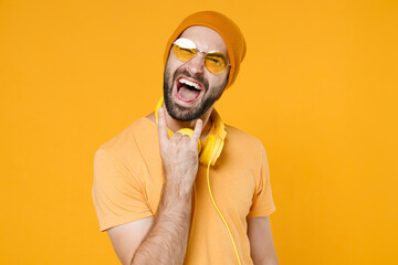 Crazy cheerful young bearded man 20s wearing basic casual t-shirt headphones eyeglasses hat...