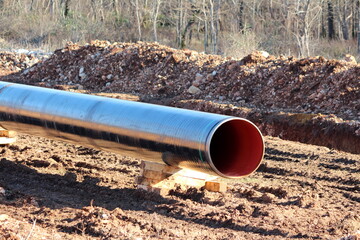 Shiny new large diameter pipe at local oil pipeline construction site supported with wooden...