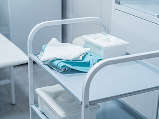 White medical operation small table bedside with towels, boxes on shelves in white interior, doctor's office. Workplace