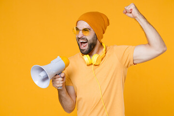 Crazy young bearded man 20s wearing basic casual t-shirt headphones eyeglasses hat standing...