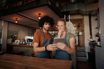 Young serious co-workers using digital tablet while standing in modern cafe