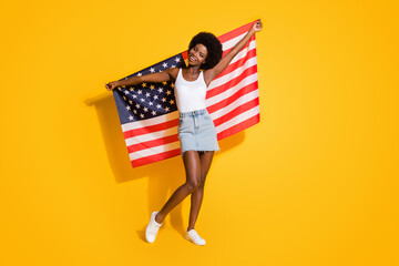 Full length body size view of pretty thin cheerful wavy-haired girl holding us flag celebrating isolated over shine yellow color background