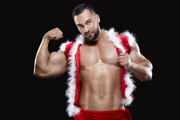 Young sexy Santa Claus in a red carnival costume on a naked body shows off his strong biceps isolated on black background