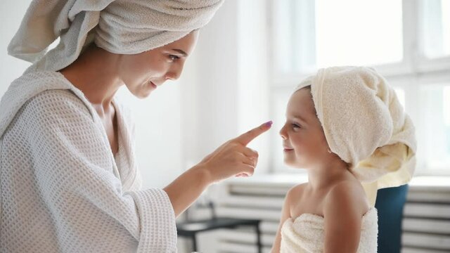 Young mother with her daughter have fun with beauty cream.