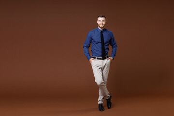 Full length of smiling confident young business man in blue shirt tie holding hands in pockets...