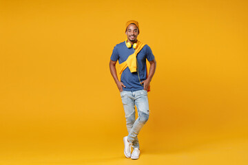 Fototapeta na wymiar Full length of smiling handsome young african american man 20s wearing blue t-shirt hat standing holding hands in pockets looking camera isolated on bright yellow colour background, studio portrait.