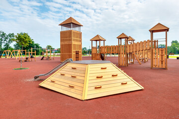 The new child playground with yellow wooden equipments and red poured in place rubber surface