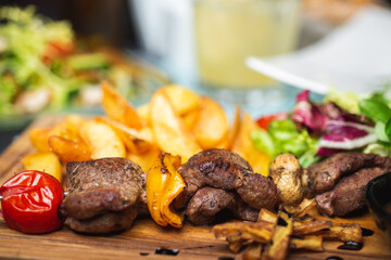 Meat, shish kebab, grilled, barbecue with baked potatoes and vegetables on a wooden plate on the table