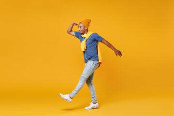 Fototapeta na wymiar Full length side view of excited young african american man 20s in blue t-shirt hat standing holding hand at forehead looking far away distance isolated on bright yellow background, studio portrait.