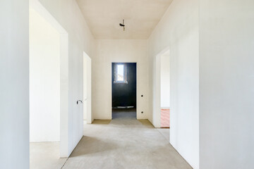 The unfinished clean hallway under construction without decoration with the white plastered walls in new building