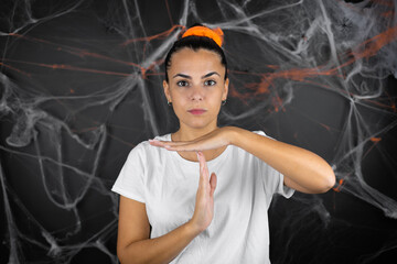 Young beautiful woman over black background with cobwebs and spiders Doing time out gesture with...