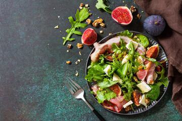 Healthy food concept. Autumn salad with figs, prosciutto, arugula, spinach, cheese, walnuts and honey on a stone countertop. Top view flat lay background. Copy space.