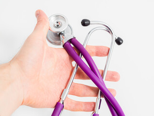 Doctor holding in hand purple violet stethoscope on white background. Close-up. Medicine