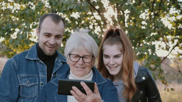 a happy old woman with her grandchildren makes a selfie or a video call to relatives at their summer cottage. Technology concept, new generation, family, communication, authenticity