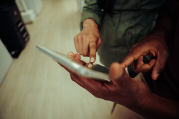 Close up of multi-ethnic co-workers working on collaboration project typing on digital tablet 