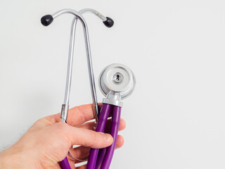 Purple colorful stethoscope in doctor's hand on white background. Close-up. Medicine