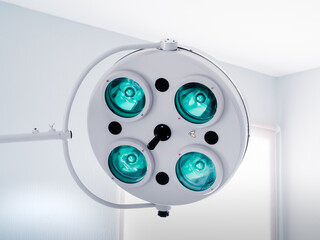 Round white swivel medical operating lamp with four green blue turquoise lights in doctor's office....
