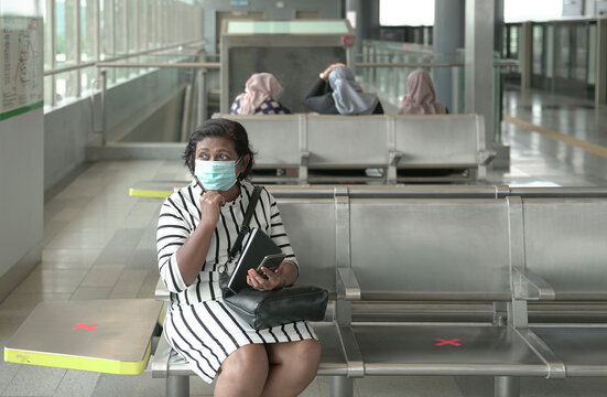 Woman wearing face mask sitting at subway station with other commuters at the background