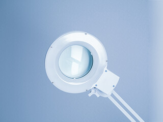 Round small white medical operating lamp in doctor's office. Light blue interier background