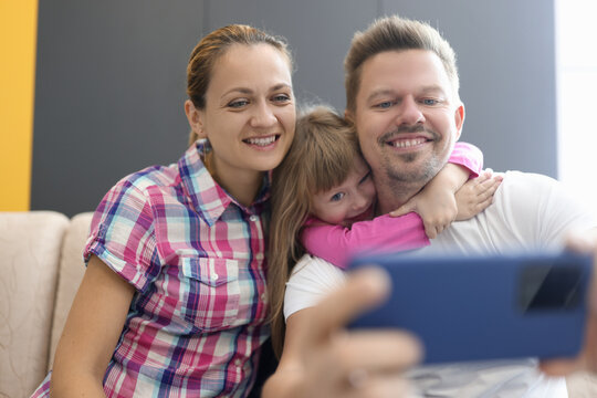 Family mom dad daughter sit in an embrace and photographed on smartphone. Family selfies for social media concept