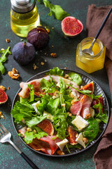 Healthy food concept. Autumn salad with figs, prosciutto, arugula, spinach, cheese, walnuts and honey on a stone countertop.
