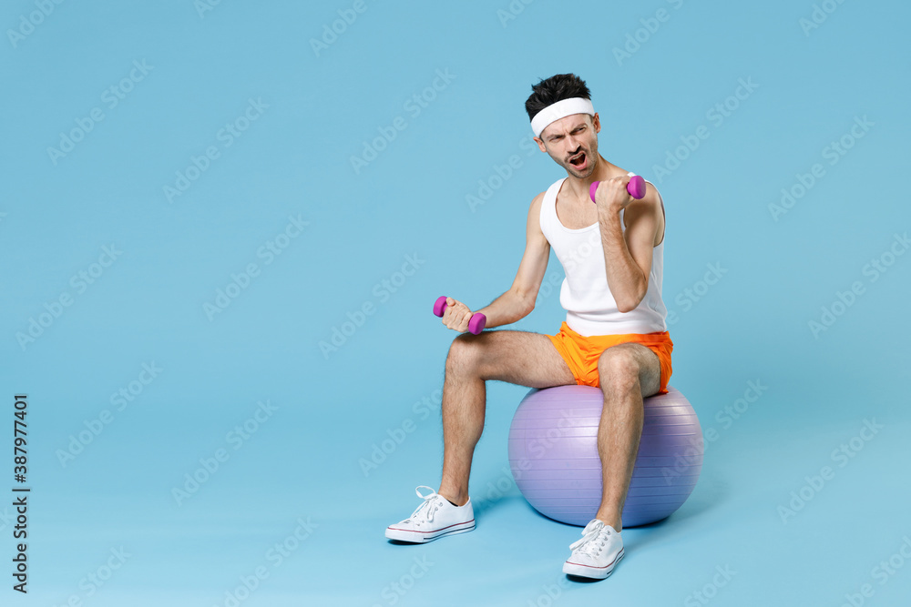 Wall mural full length portrait of strong man with skinny body sportsman in headband shirt shorts sit on fitbal