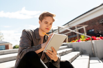 leisure, education and people concept - young man or teenage boy with notebook, diary or sketchbook...