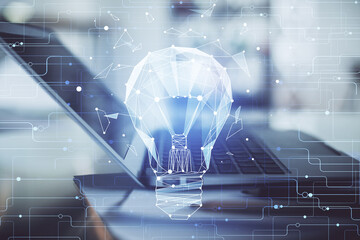 Computer on desktop in office with bulb icon hologram. Double exposure. Concept of idea.