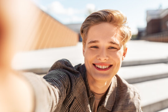 leisure, technology and people concept - happy smiling nice young man or teenage boy taking selfie in city