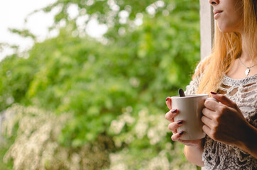 woman's hands with a cup of tea in front of the window on a gray day