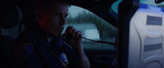 Police officer talking on CB radio while checking info on a laptop inside a car