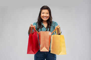 sale, outlet and consumerism concept - happy asian young woman with shopping bags over grey background