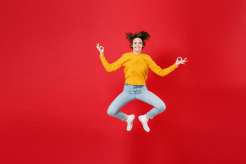 Fototapeta na wymiar Full length of smiling young brunette woman 20s in basic yellow sweater jumping hold hands in yoga gesture relaxing meditating trying to calm down isolated on bright red background studio portrait.